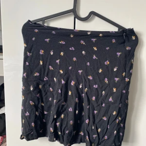 Svart blommig kjol - Svart kortkjol med små blommor i lila, gult och vitt. Kjolen har en mer tajtare fit och är perfekt att styla med ett linne eller en fin blus. PERFEKT för sommaren och är jätte snygg😍