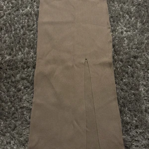 Beige ribbad långkjol med slits - Säljer en beige ribbad långkjol med en snygg slits framtill. Kjolen har en rak passform och är perfekt för dig som gillar en stilren och enkel look. Passar till många olika outfits! Lite noppig på baksidan 