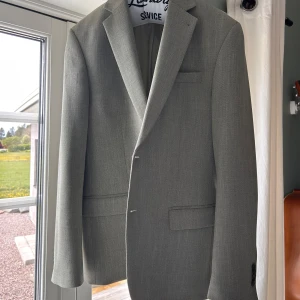 Ljusgrön kavaj från Dressmann - Snygg ljusgrå kavaj från Dressmann i slim fit-modell. Kavajen har klassiska slag, två framfickor med lock och en bröstficka. Perfekt för dig som vill ha en stilren och modern look.
