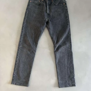Grå Levi's 501 jeans - Säljer ett par klassiska grå Levi's 501 jeans med raka ben och femficksmodell. Jeansen har knappgylf och är tillverkade i slitstarkt denim. Perfekta för dig som gillar en tidlös och avslappnad stil.