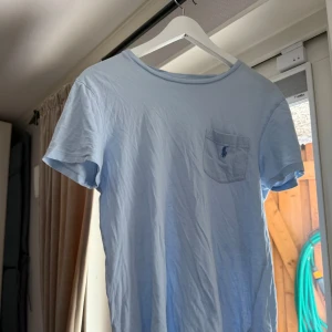 Ljusblå t-shirt från Polo Ralph Lauren - Säljer en ljusblå t-shirt från Polo Ralph Lauren med klassisk rund hals och liten bröstficka med broderad logga. T-shirten är kortärmad och tillverkad i mjuk bomull. Perfekt för en avslappnad stil.