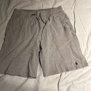 Grå shorts från Polo Ralph Lauren - Säljer ett par ljusgrå shorts från Polo Ralph Lauren med snörning i midjan och fickor på sidorna samt en bakficka. Klassisk broderad logga i mörkblått på ena benet. Perfekta för sommaren och tillverkade i mjuk bomull.