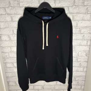 Ralph Lauren hoodie - Stilren hoodie i svart med klassisk röd Polo-logga. Använd endast en gång och är i princip helt nyskick. Mjuk och skön modell med huva och känguruficka. Hör av dig vid intresse! 🙌