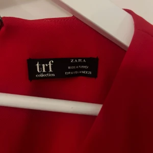 Röd klänning med v-ringning från Zara - Säljer en röd klänning från Zara TRF Collection med v-ringning och korta ärmar. Klänningen har en rak passform och dragkedja i ryggen. Perfekt för dig som gillar enkel men snygg stil.