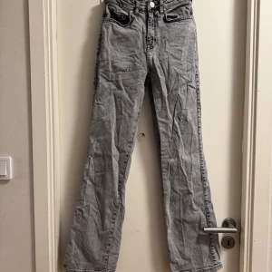 Grå raka jeans - Säljer ett par grå jeans med raka ben och klassisk femficksdesign. Jeansen har hög midja och stängs med dragkedja och knapp. Perfekta till en avslappnad stil och passar till många olika outfits.