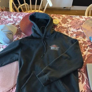 Svart Outkast hoodie med tryck - Svart hoodie med stor Outkast Stankonia-tryck på ryggen och mindre logga på bröstet. Klassisk huva med dragsko och känguruficka framtill. Perfekt för dig som gillar hiphop och streetwear. S men passar som M