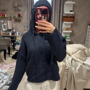 Mörkblå hoodie i mjukt material - Säljer en mörkblå hoodie med luva och dragsko. Tröjan är i ett mjukt, lite fluffigt material och har en avslappnad passform. Perfekt för en chill och bekväm stil.