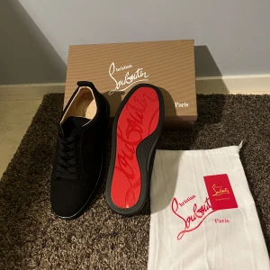 Svarta sneakers från Christian Louboutin - Säljer ett par svarta sneakers från Christian Louboutin med klassisk röd sula och diskret logga. Skorna har snörning och är tillverkade i en kombination av skinn och syntetmaterial. Perfekta för dig som vill ha en stilren och lyxig look.