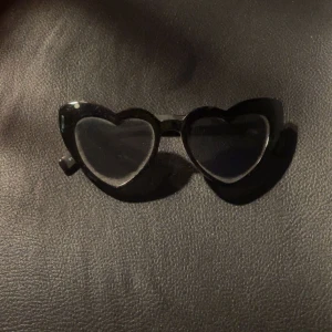 Svarta hjärtformade solglasögon - Säljer ett par svarta solglasögon med hjärtformade bågar. Glasögonen har en cool och lekfull design som sticker ut och passar perfekt för dig som vill ha något unikt.