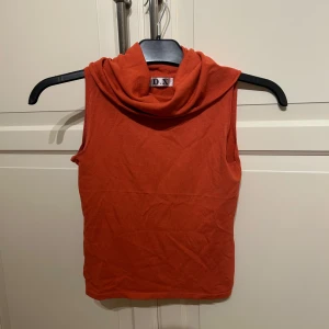 Orange ärmlös polotopp från D.X - Säljer en snygg orange ärmlös polotopp från D.X i strl S. Toppen har en hög polokrage och är i ett mjukt material som känns skönt mot huden. 