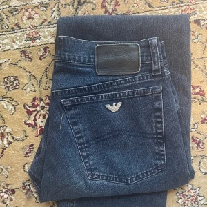 Mörkblå jeansbyxor från Armani - Säljer ett par mörkblå jeansbyxor från Armani med klassisk femficksdesign och silverfärgad logga på bakfickan. Jeansen har normal passform och raka ben. Perfekta för dig som gillar stilrena och tidlösa jeans.