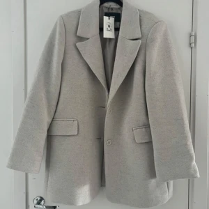 Ljus beige kavaj från Bik Bok - Säljer en stilren ljus beige kavaj från BikBok med klassisk krage och två fickor framtill. Jackan har lång ärm och stängs med knappar. Perfekt för dig som vill ha en enkel och snygg look.  Storlek L. Ny med prislapp. Nypris 999kr