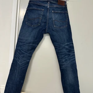 Mörkblå jeansbyxor från Replay - Säljer ett par mörkblå jeans från Replay med klassisk femficksdesign och snygga slitningar på framsidan. Jeansen har normal passform och raka ben. Perfekta för dig som gillar en tidlös stil med lite edge.
