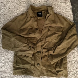 Olivgrön overshirt från Replay - Säljer en olivgrön overshirt från Replay med klassisk krage och stora bröstfickor. Jackan har knäppning framtill och är tillverkad i ett kraftigare bomullstyg. Perfekt att slänga över en t-shirt för en avslappnad look.