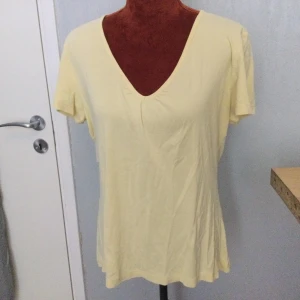 Ljusgul t-shirt med v-ringning L - En enkel ljusgul t-shirt med v-ringad hals och korta ärmar. Tillverkad i 100% bomull vilket gör den mjuk och skön att bära. Passar perfekt till vardags och är lätt att matcha med andra plagg. Uppskattad storlek: L. Katter finns i hemmet! 