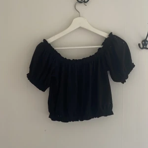Svart croppad blus från Gina Tricot - Säljer en svart croppad blus från Gina Tricot med puffärmar och resår vid halsringning och midja. Toppen har en offshoulder-design och är perfekt för en trendig look.