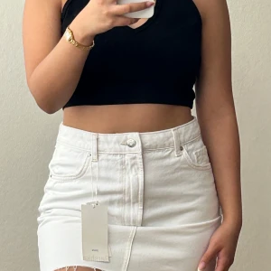 Vit jeanskjol från Bershka - Snygg vit jeanskjol från Bershka i klassisk femficksmodell. Kjolen har rå kant nedtill, bälteshällor och knappstängning framtill. Passformen är normal och materialet är stadigt denim. Aldrig använt!