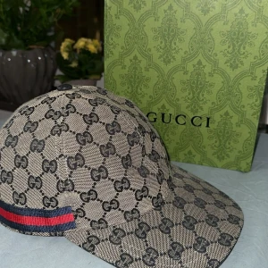 Gucci beige keps med GG-mönster - Säljer en snygg beige keps från Gucci med det klassiska GG-monogrammet i svart över hela kepsen. Äkta från England, box kommer med. Använd 3 gånger