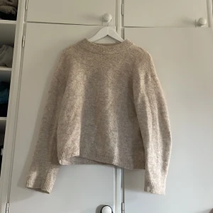 Beige stickad tröja från H&M - Mysig beige stickad tröja från H&M i ull- och alpackablandning. Tröjan har en rund hals, ribbade muddar och långärmad passform. Perfekt för dig som gillar en enkel och chill stil med lite oversized känsla.