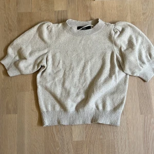 Beige stickad tröja Vero Moda XS - Säljer en beige stickad tröja från Vero Moda i storlek XS. Tröjan har puffiga korta ärmar och ribbad kant vid hals, ärmslut och nederkant. Perfekt för dig som gillar en enkel men trendig look med lite volym på axlarna.