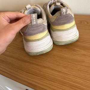 Levi's sneakers i vitt och pastell - Levis® West-sneakers i klassisk vit farg, storlek 39. Skorna ar i gott skick bade invändigt och utvändigt. Pa insidan av hälen finns en liten härd del i materialet som kan skava mot foten. Det gar lätt att lösa med ett halskydd, men eftersom storleken är exakt sa blev skorna för tranga för mig när jag anände det. Passar perfekt för dig med storlek 38 - köp till ett enkelt hälskydd sa blir de bade bekväma och snygga!