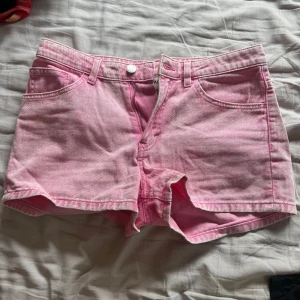 Rosa jeansshorts  - Snygga rosa jeansshorts med klassisk femficksdesign och bälteshällor. De har en ljus tvätt och stängs med knapp och dragkedja framtill. Perfekta för varma dagar och ger en cool vibe till din outfit.