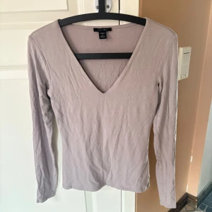  långärmad topp från Amisu - Säljer en långärmad topp från Amisu med djup v-ringning. Toppen är figurnära och har en enkel, stilren design. Lite lila/grå i färgen. 