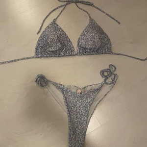 Blommig blå bikini  - Supersöt bikini med ljusblå och vita blommor. Triangeltopp med knyt i nacken och ryggen, samt matchande trosa med knyt i sidorna. Materialet är mjukt och stretchigt, perfekt för strandhäng. Fräsch och trendig look för sommaren!