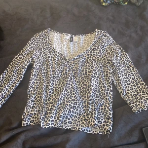 Leopardmönstrad trekvartsärmad topp H&M - Säljer en snygg trekvartsärmad topp från H&M med leopardmönster i svart och beige. Toppen har v-ringad hals och är tillverkad i mjuk och tunn bomull, perfekt för dig som gillar att sticka ut med djurmönster. Passar dig som vill ha en cool och trendig look.