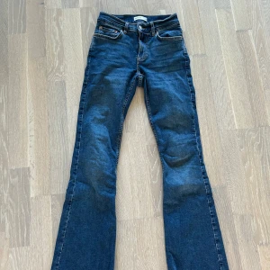 Blå bootcut jeans från Gina Tricot - Snygga blå jeans från Gina Tricot i modellen bootcut. Klassisk femficksdesign, normal passform och tillverkade i mjukt bomullstyg. Perfekta för dig som gillar en retrovibe med utsvängda ben och tidlös denimlook.