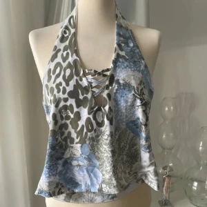 Blommig halterneck topp Glitzy London - Supersnygg halterneck topp från Glitzy London med blått och grönt blommönster och inslag av leopard. Toppen har snörning framtill och är croppad med öppen rygg. Perfekt för dig som vill sticka ut med en unik mix av mönster och färger.