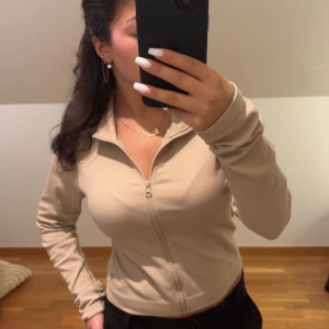 Beige ribbad zipjacka från Guess - Säljer en beige ribbad zipjacka från Guess med hög krage och hel dragkedja framtill. Jackan har långärmade ärmar och en croppad passform som sitter snyggt på kroppen. Perfekt för dig som gillar stilrena och enkla plagg med en sportig vibe. För att jämföra så brukar xs sitta tajt på mig men eftersom den ska sitta tajt så sitter en L rätt så fitted ändå. Den är aldrig använd men har inga prislappar. Pris kan diskuteras 