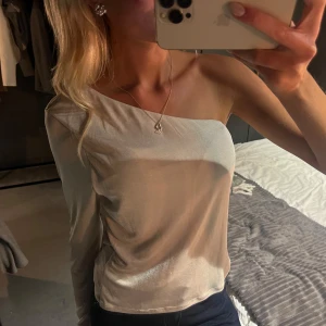 Champagnefärgad oneshoulder topp - Snygg och stilren champagnefärgad topp med oneshoulder-design och lång ärm på ena. Från MQ🌸