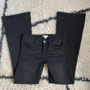 Gina Tricot jeans - Ett par jätte snygga Svarta jeans från Gina young i bootcut lågmidjade med snygga silverfärgade nitar på bakfickorna, midjemått 36cm rakt över innerbensmåttet 80cm, Materialet har lite stretch också.
