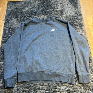 Grå sweatshirt från Nike - Säljer en stilren grå sweatshirt från Nike i storlek M. Tröjan har en klassisk rund hals, långa ärmar och en liten vit Nike-logga på bröstet. Mjuk insida i fleece som gör den extra skön. Perfekt för chill dagar eller när du vill ha en enkel look.