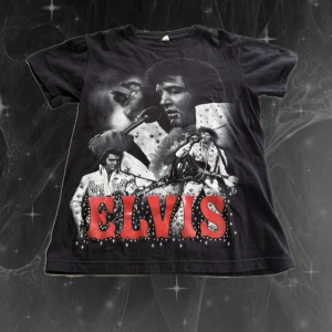 Svart Elvis t-shirt med tryck - Svart t-shirt med stort Elvis-tryck i rött och vitt på framsidan och baksidan. Klassisk rund hals och korta ärmar. Materialet är mjuk bomull och passformen är normal. Perfekt för dig som älskar retro och musikikoner.