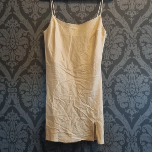 Beige linneklänning från ASOS Design - Säljer en stilren beige kortklänning från ASOS Design i linne. Klänningen har smala axelband, rak passform och en liten slits nedtill. Perfekt för varma dagar och enkel att styla med accessoarer. Storlek EU 38. Vi kan prata om priset