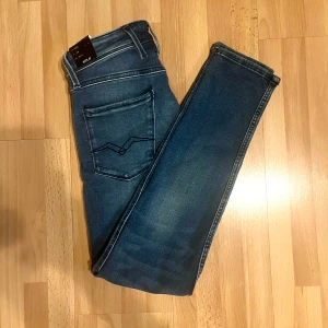 Replay Anbass blå jeans med power stretch - Snygga Replay Anbass jeans i en klassisk blå tvätt med power stretch för extra komfort. Modellen har fem fickor, smal passform och raka ben. Jeansens material är en blandning av bomull och syntet, vilket ger dem en mjuk och flexibel känsla. Perfekt för dig som gillar stilrena och moderna jeans. Är små i storleken.