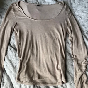 Beige långärmad topp Gina Tricot - En stilren beige långärmad topp från Gina Tricot med rundad, djup ringning och liten slits vid ärmsluten. Tunn och mjuk 