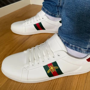Gucci ace vita  - Säljer ett par helt nya Gucci Ace vita sneakers i storlek 43. 	                                                                          •	Oanvända och i nyskick 	                                               •	Påse, box och extra skosnören ingår                 Väldigt populära och efterfrågade skor från Gucci.   OBS!!! Inte helt säker på äktheten (därav priset).      Det är bara att skriva vid funderingar eller om du vill ha fler bilder.
