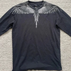 Marcelo Burlon svart långärmad tröja - Storlek S sitter mer som M. Svart äkta långärmad  tröja från Marcelo Burlon med ikoniskt fjädermönster i grått runt halsen och axlarna, både fram och bak. Tröjan är gjord i mjuk bomull och har en normal passform. 