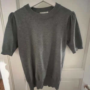 Grå stickad tröja Saint Tropez S - Snygg grå stickad tröja från Saint Tropez i storlek S. Modellen har korta puffärmar och bred ribbad halsringning. Perfekt för dig som gillar enkel och stilren design med en liten twist på ärmarna. Mjuk och skön kvalitet som passar till många outfits.