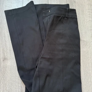 Svarta kostymbyxor från NA-KD - Snygga svarta kostymbyxor från NA-KD i storlek 34. Byxorna har klassisk rak passform med midja och bälteshällor. Perfekta för en clean och stilren look, passar till skjorta eller t-shirt. Materialet känns mjukt och har en lätt stretch för extra komfort.