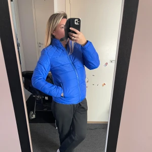 Blå pufferjacka med dragkedja - Säljer en snygg blå pufferjacka med hög krage och praktiska sidofickor med dragkedja. Jackan har quiltade detaljer upptill och är tillverkad i ett syntetmaterial som håller värmen. Perfekt för dig som gillar en sportig och clean look.Helt ny