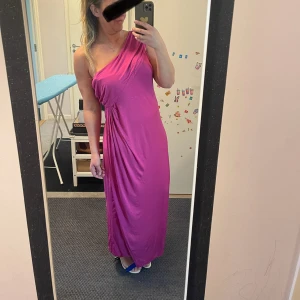 Lång rosa oneshoulder klänning läs om storlek  - Säljer en snygg lång klänning i stark Rosa-lilla färg med oneshoulder-design. Klänningen har draperade detaljer över axeln och midjan som ger en cool och elegant look. Materialet är mjukt och har ett fint fall, perfekt för att sticka ut.Finns i två storlek 42/44 och 38/40 (som är på bilder) helt nya