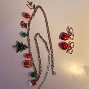 Juligt halsband och örhängen med charms - Säljer ett festligt halsband med juliga berlocker som julgran, paket, julstrumpa och bjällror i rött, grönt och silver. Till setet hör ett par örhängen med röda hjärtan och polkagrisrosetter. Perfekt för dig som vill maxa julstämningen med färgglada detaljer! Är öppen på prisförslag!💓