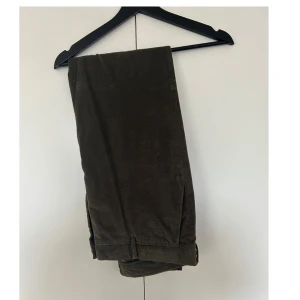 Bruna/gröna manchesterbyxor från Massimo Dutti - Snygga bruna/gröna manchesterbyxor från Massimo. Byxorna har klassisk design med bälteshällor och är tillverkade i mjukt manchestertyg som ger en cool vintagekänsla. Perfekta för dig som gillar stilrena och bekväma byxor.