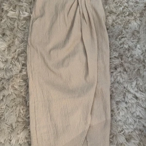 Beige omlottkjol från H&M - Säljer en beige omlottkjol från H&M i storlek XS. Kjolen har en snygg omlott-design och är gjord i ett strukturerat, lätt och skönt polyestermaterial. Perfekt för dig som gillar en enkel men trendig look med lite textur. Passar dig som vill ha en neutral ton i garderoben. Aldrig använd