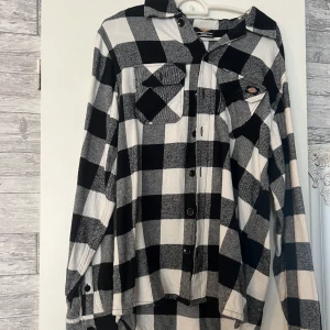 Svartvit rutig skjorta från Dickies - Snygg svartvit rutig skjorta från Dickies i storlek small. Skjortan har klassisk krage, två bröstfickor med knappar och tydliga Dickies-loggor. Perfekt för dig som gillar streetwear och vill ha en chill look.