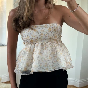 Blommig bandeau tubtopp med volang - Supersöt topp med blommigt mönster i ljusgult och beige. Toppen har volang nedtill och öppen rygg med snörning baktill. Har sytt den själv så den är inte perfekt! Skulle säga strl XS//S. Den går att justera efter behov i ryggen 🥰